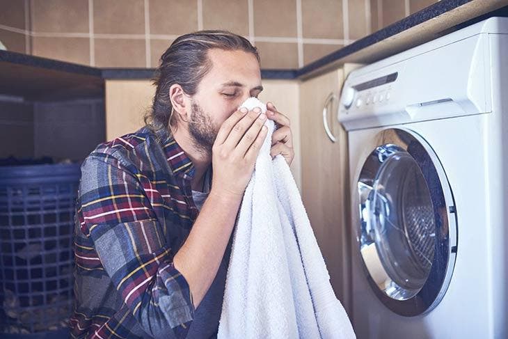 Mann schnuppert den angenehmen Geruch seiner Wäsche frisch aus der Waschmaschine